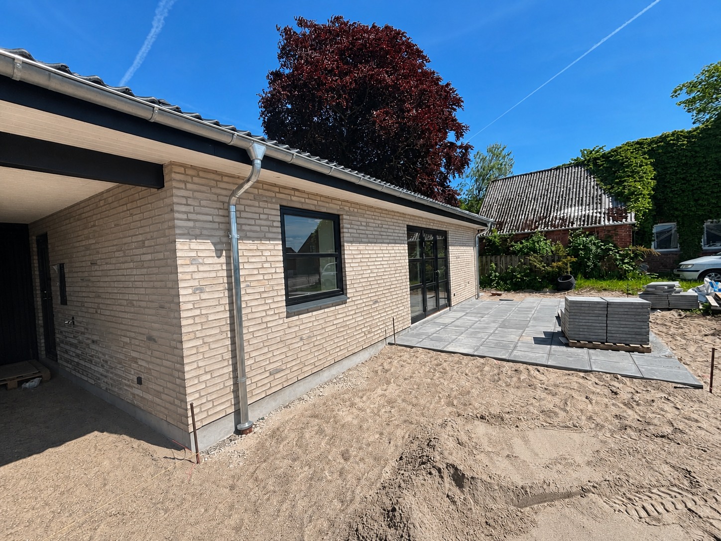 Lys murstensfacade med sorte vinduer og carport